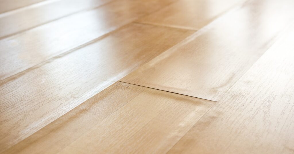 A close-up of laminate wood-style flooring. The edges are swelling and bent, indicating moisture below the floor.